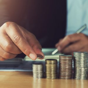 concept saving money. hand holding coins putting stack on table in office