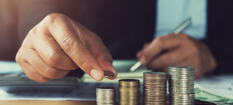 concept saving money. hand holding coins putting stack on table in office